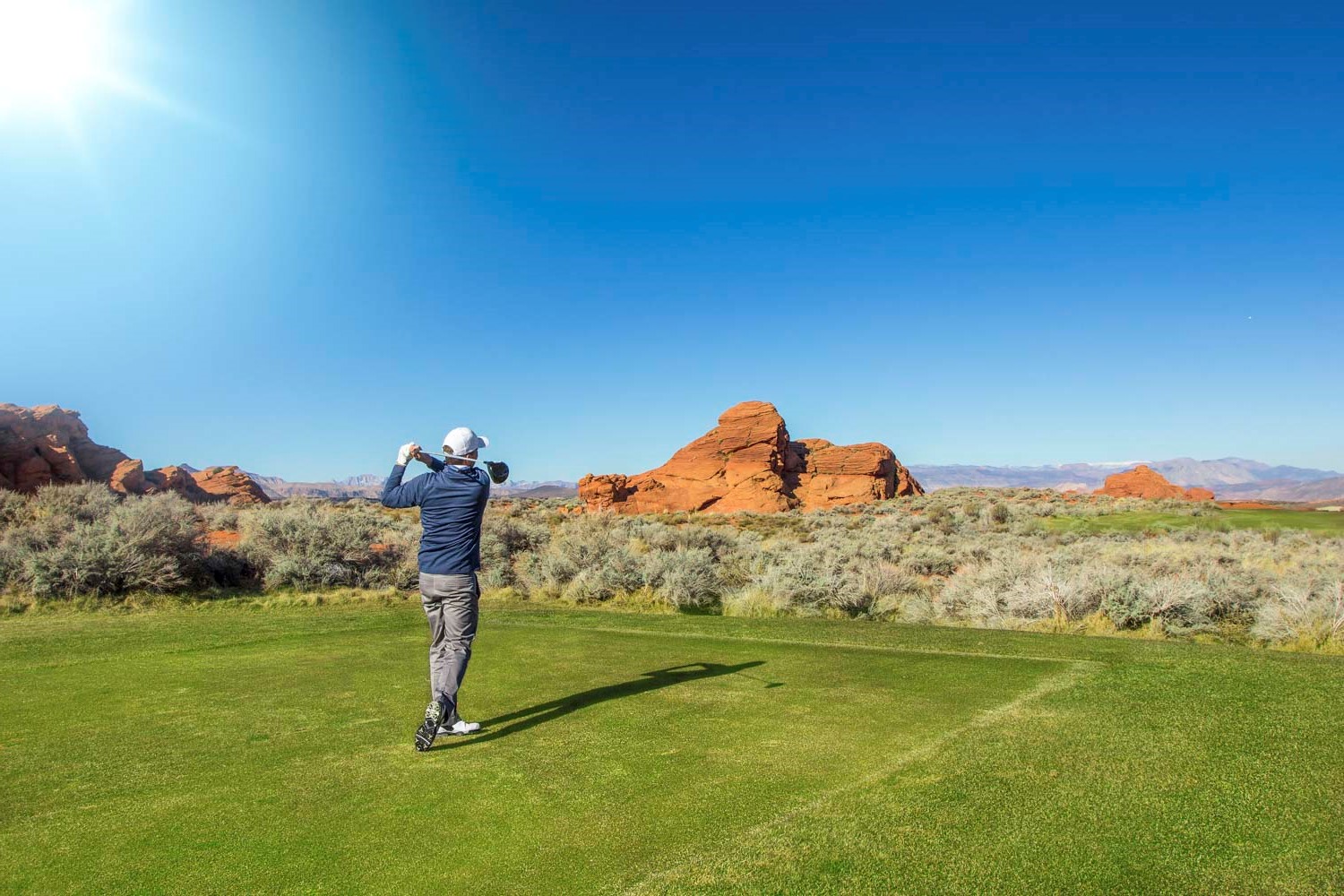Golfer mid-swing on a desert golf course with red rock formations and a clear blue sky in apache junction az