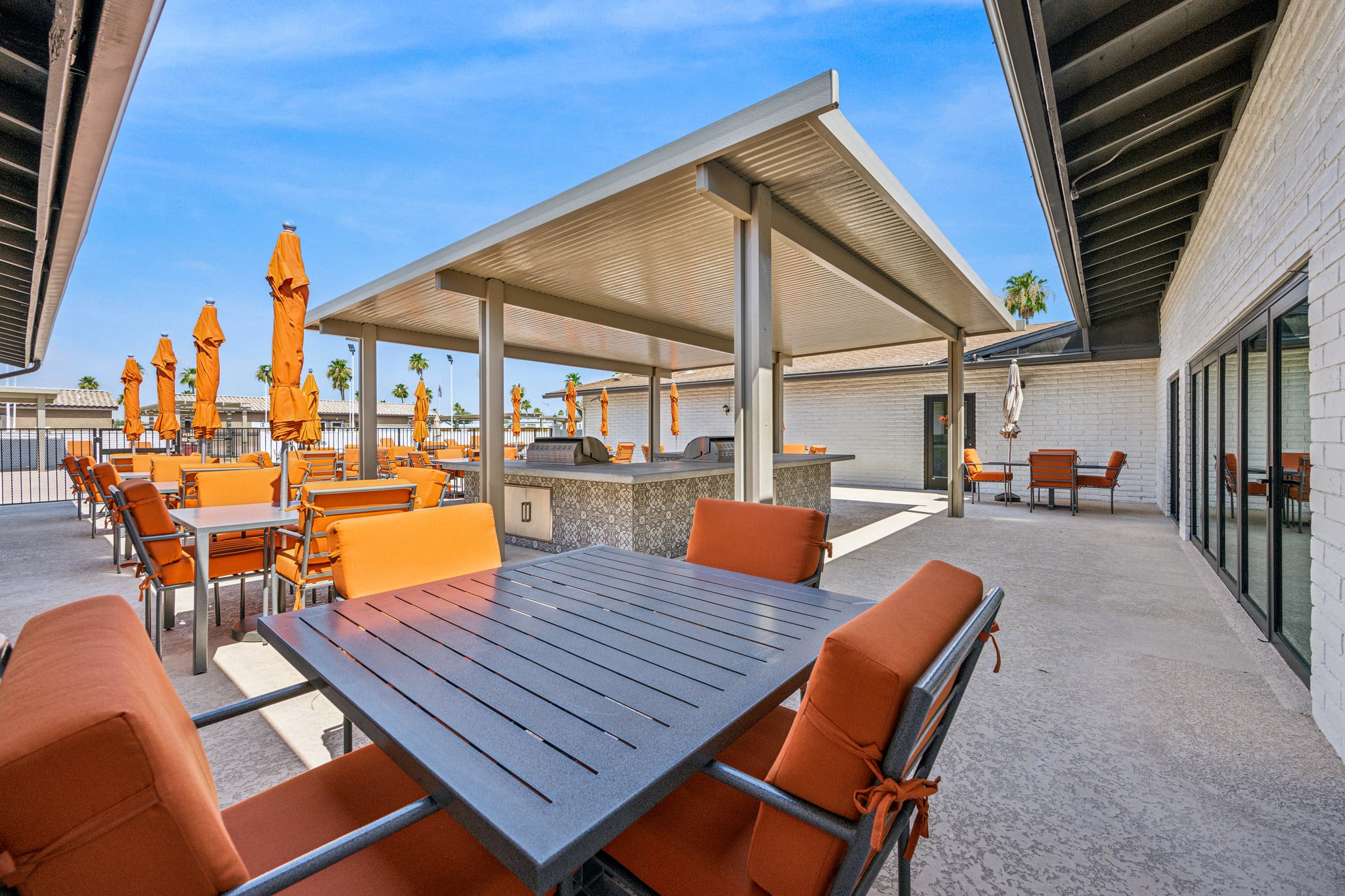 Outdoor patio dining area with orange cushioned chairs, large umbrellas, and a covered grill space in apache junction az